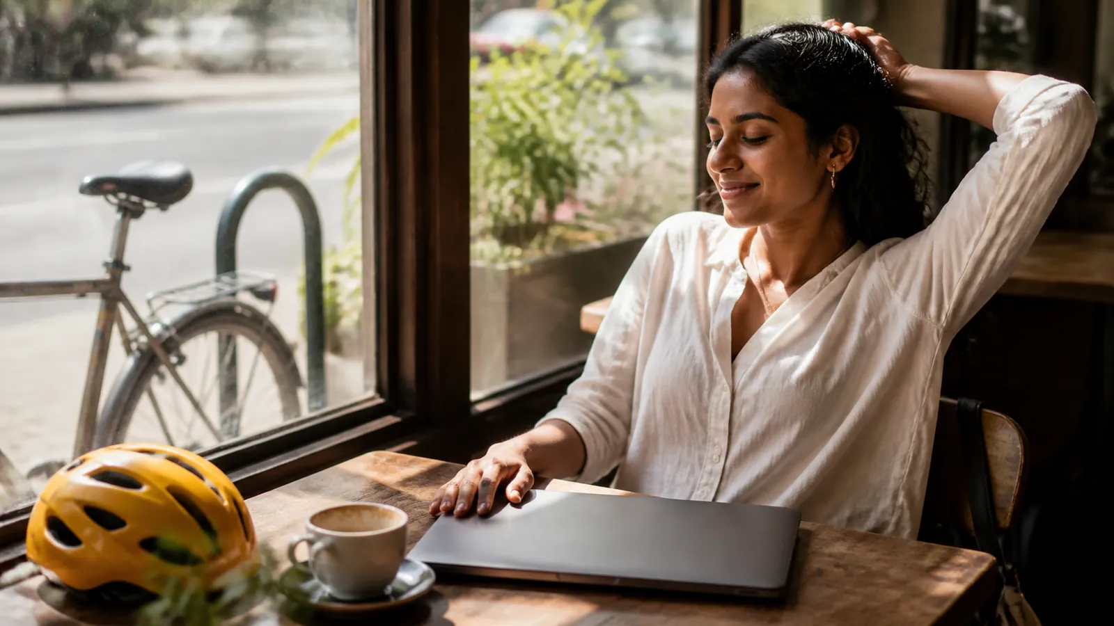 Freelancer closing her laptop with a satisfied stretch at a sunny cafe window table